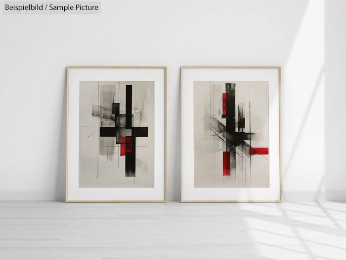 Two framed abstract paintings with black and red geometric shapes on a light background, leaning against white wall.