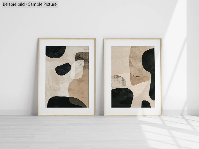 Two framed abstract prints with black, beige, and cream shapes, displayed on a white wall with sunlight casting shadows.