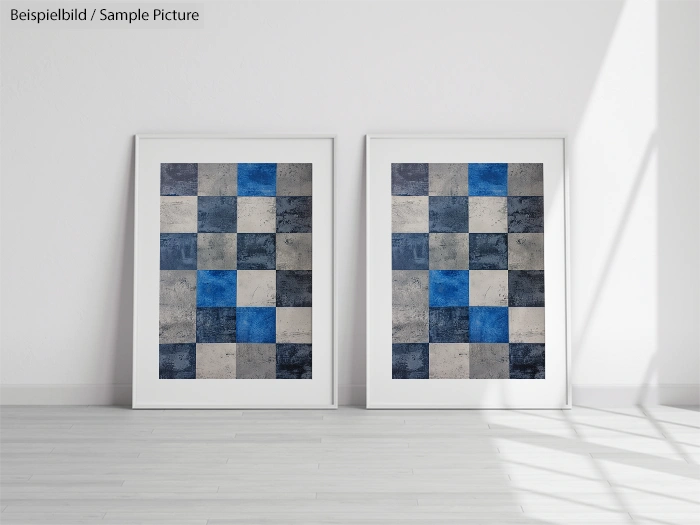 Two framed abstract artworks with blue, grey, and white squares, leaning against a white wall.