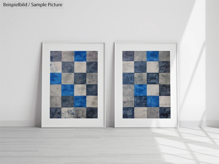 Two framed mosaic art pieces with blue and gray tiles on a white floor against a white wall.