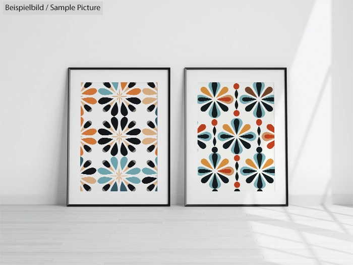 Two framed geometric art prints with bold colorful patterns, leaning against a white wall on a wooden floor.