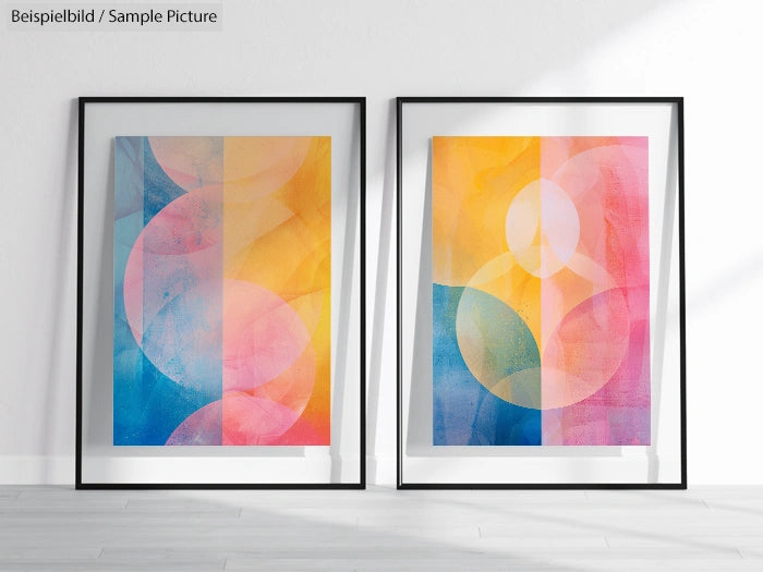 Two abstract paintings with circular patterns in vibrant orange, pink, and blue shades, framed and displayed on a floor.