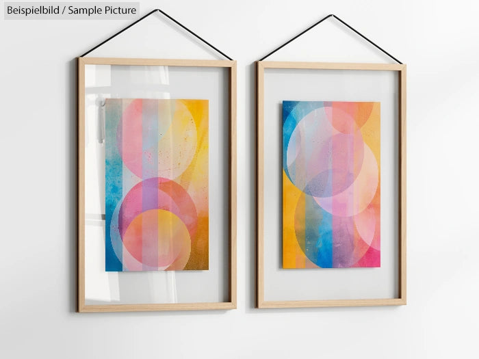 Two abstract artworks in frames with colorful overlapping circles, hanging on a white wall.