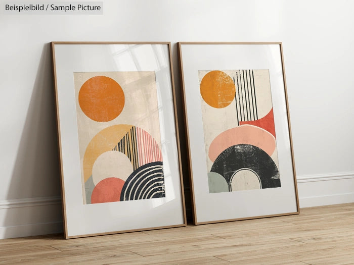 Two modern abstract art prints with geometric shapes in orange, pink, and black, framed and leaning against a wall.