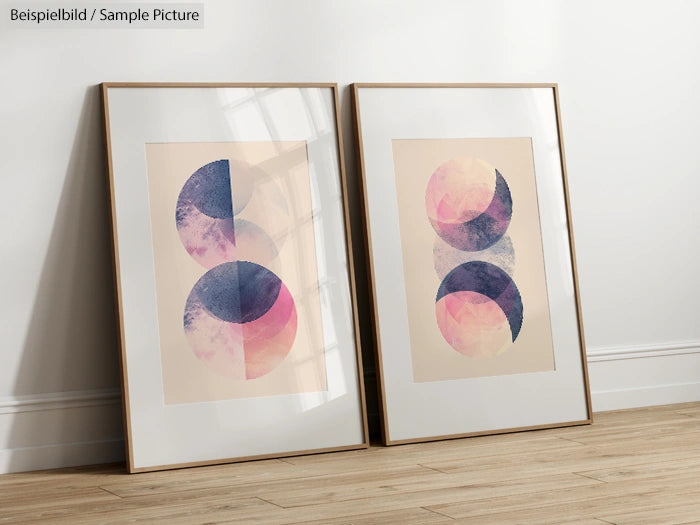 Two framed abstract art prints with geometric circles in blue and pink hues, leaning against a white wall on a wooden floor.