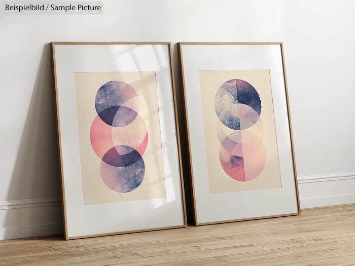 Two framed abstract art prints with overlapping geometric circles in pink, purple, and blue hues, leaning on a wall.