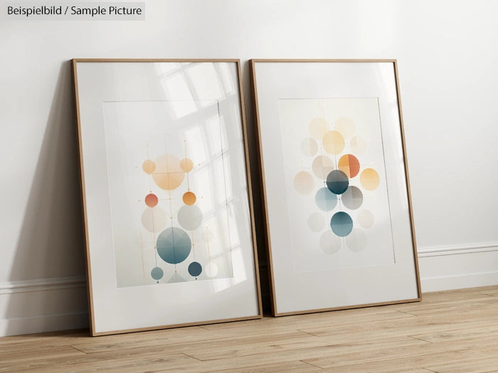 Two framed abstract art prints with colored circular patterns leaning against a white wall on a wooden floor.