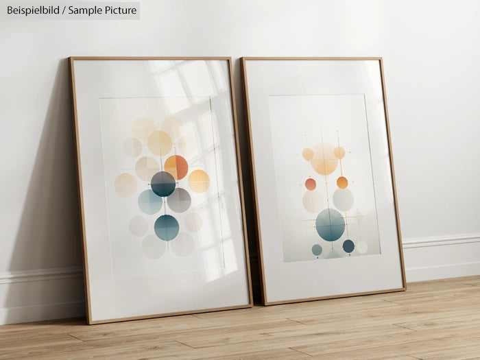 Two framed abstract geometric artworks with circles, leaning against a wall on a wooden floor.