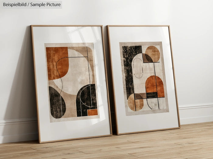 Two framed abstract geometric art prints with earthy tones leaning against a white wall on a wooden floor.