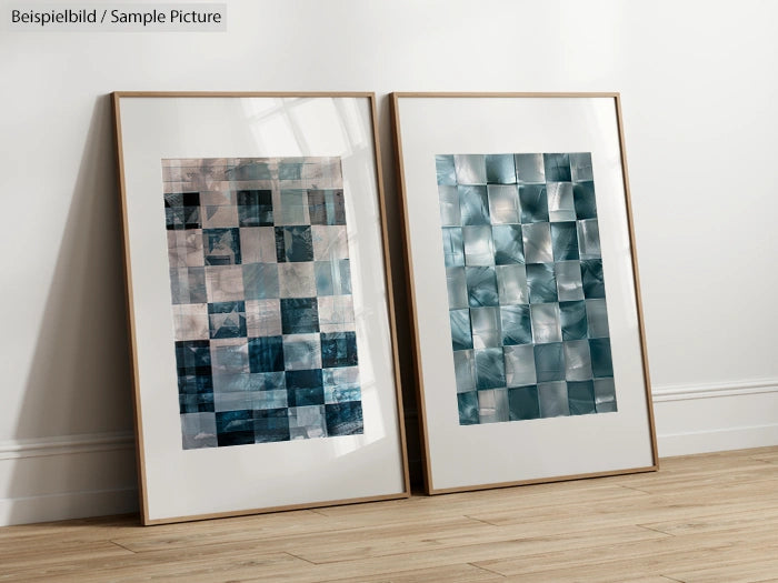 Two framed abstract art pieces with blue square patterns leaning against a white wall on a wooden floor.