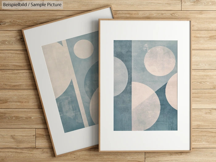 Two abstract geometric prints with blue and beige circular patterns in wooden frames on a wooden floor.