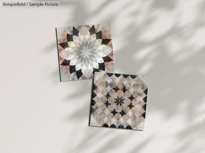 Two square tiles with intricate geometric patterns in earthy tones, casting shadows on a neutral background.