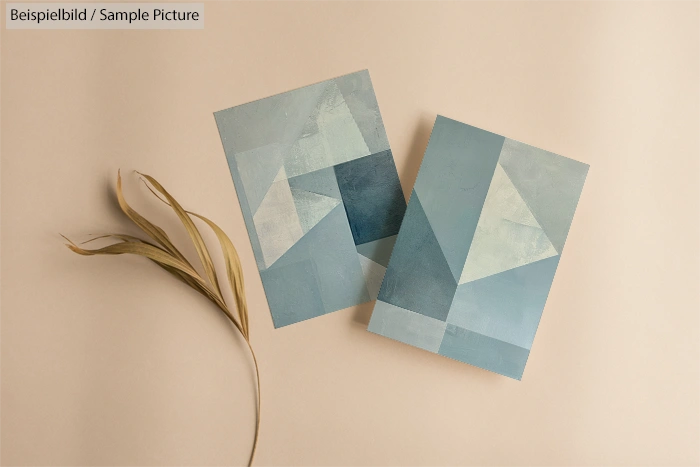 Two abstract geometric paintings in soft blue and green tones on a beige background with a dried grass accent.