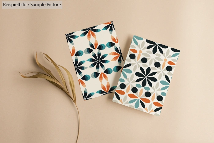 Two geometric pattern cards on beige surface with dried leaf.