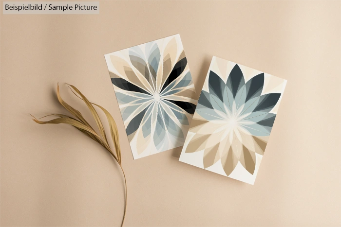 Two geometric floral pattern posters on beige background next to a dry leaf. One is blue-toned, the other beige-toned.