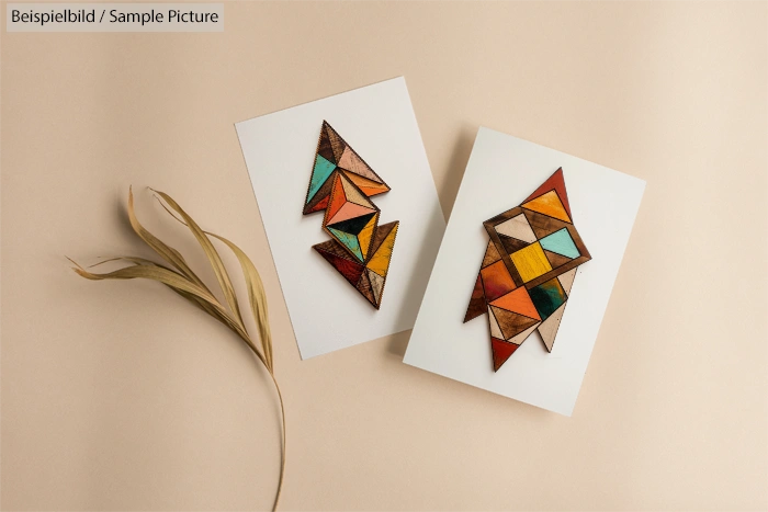 Geometric stained glass artworks on paper with decorative plant leaf on a beige background.