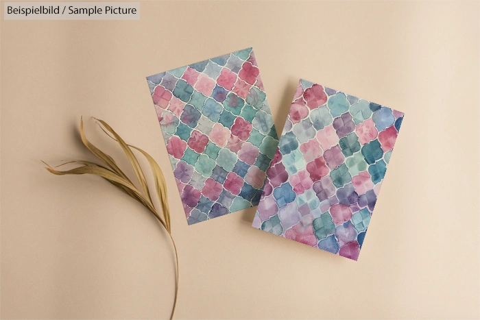 Two watercolor pattern cards on beige background beside dried grass sprigs.