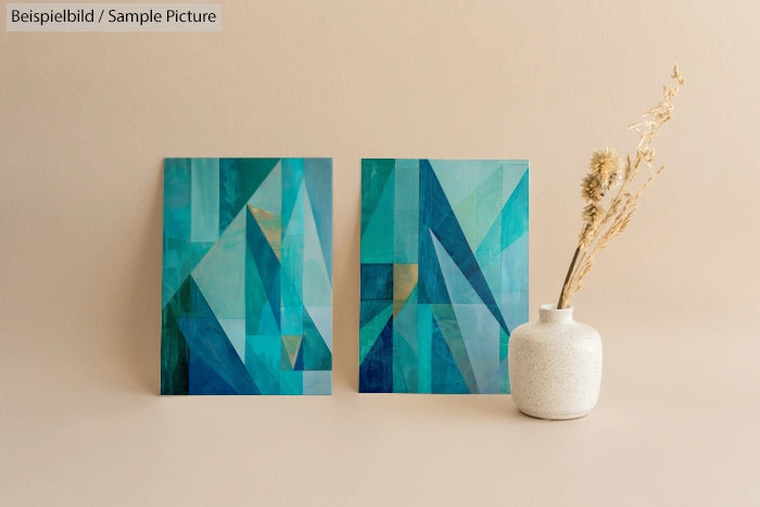 Two abstract teal and blue paintings next to a white vase with dried flowers on a beige background.