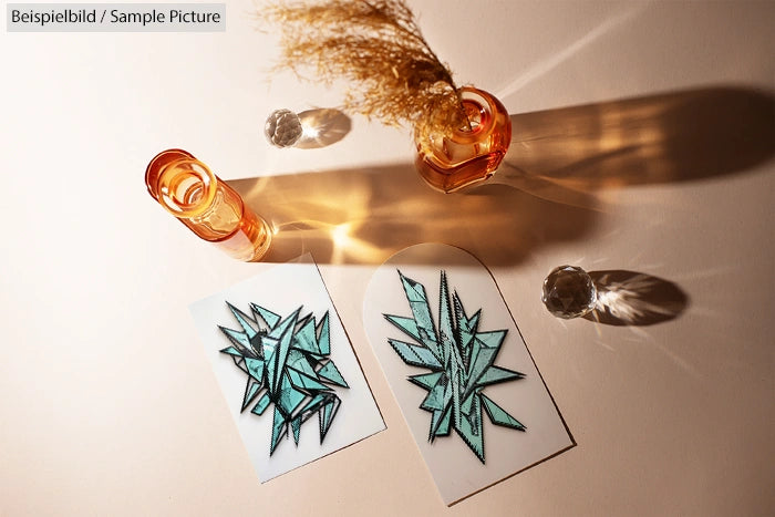 Geometric plant art prints on table with orange glass bottles casting shadows.