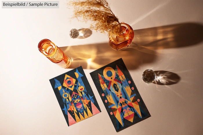 Geometric abstract art pieces on table with orange glass vases casting shadows.