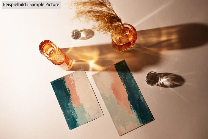 Two abstract paintings in teal and peach tones with vases and shadows on a white surface under warm lighting.