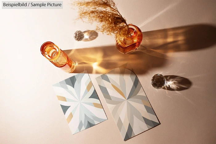 Two geometric patterned cards on a light surface, beside amber glass vases casting soft shadows.