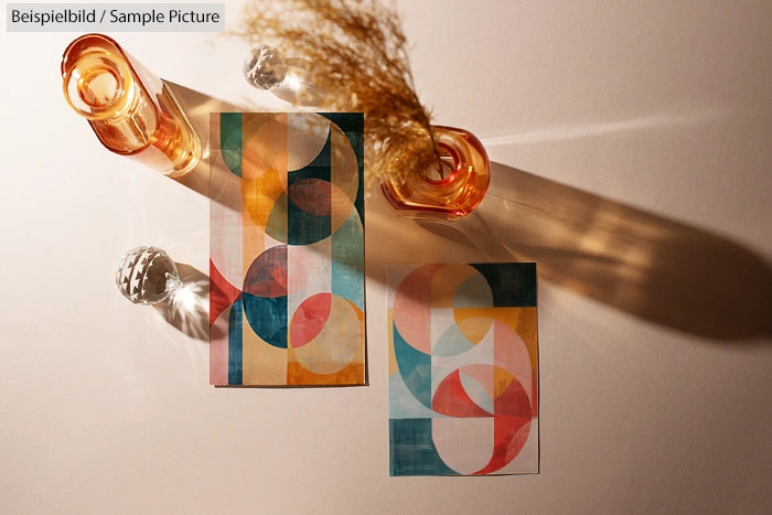 Geometric abstract art with circular shapes in warm tones, placed near glass vases casting shadows on a white surface.