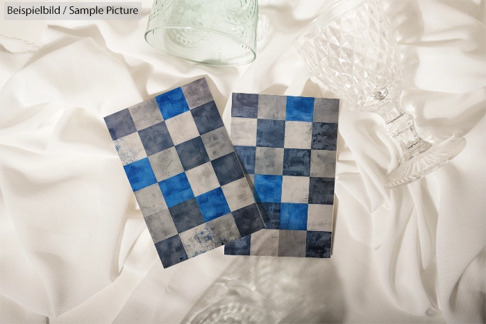 Two checkered tile samples in blue and gray on white fabric, surrounded by crystal glasses.