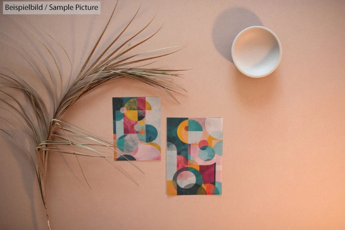 Abstract art cards with colorful geometric shapes on a beige background with a dried plant and a white bowl.