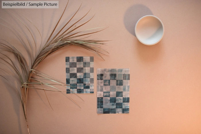 Two checkered paper sheets and leaves on a beige surface, with a white bowl casting a shadow.