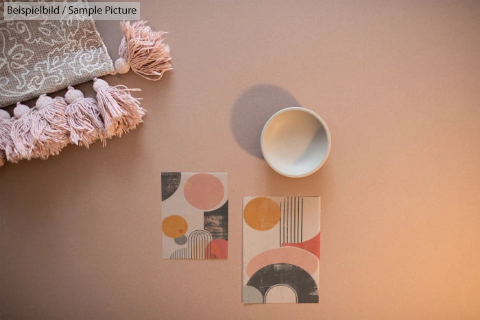 Flat lay of postcards, bowl, and tasseled blanket on a neutral surface with warm lighting.