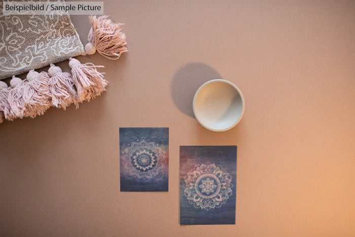 Flat lay of bohemian art prints, a ceramic bowl, and a tasseled fabric on a neutral background.