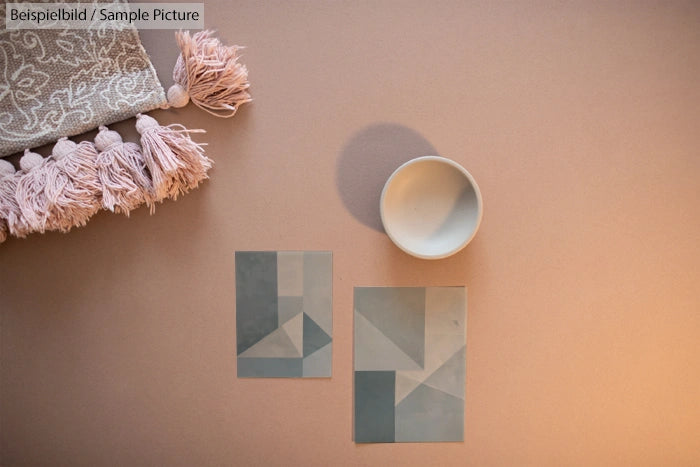 Soft pink towel with tassels, geometric tiles, and a white bowl on a beige background.