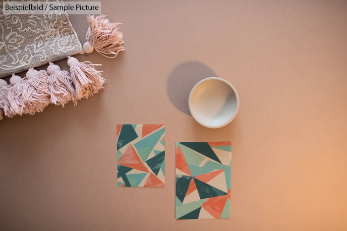 Geometric art prints with orange, teal, and beige shapes next to a bowl and tasselled fabric.