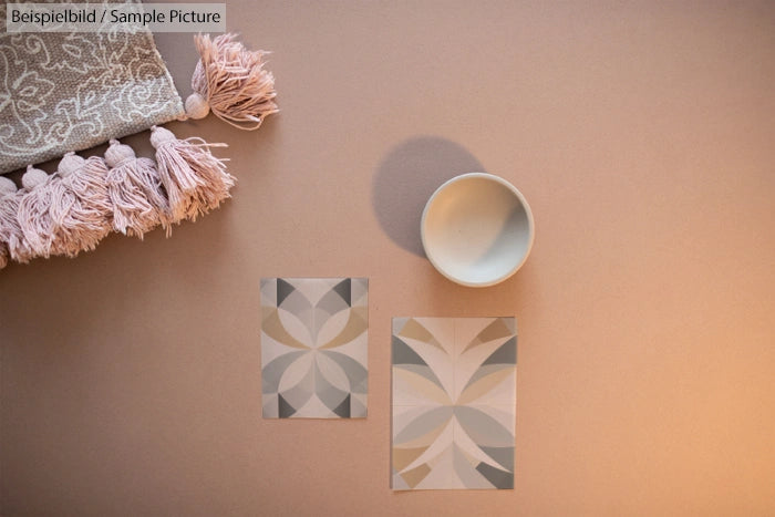 Flat lay of decorative cards, ceramic bowl, and textured fabric with tassels on a beige surface.