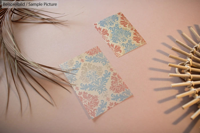 Two ornate cards with pink and blue floral patterns on a beige background, surrounded by dried plants and a rattan mat.