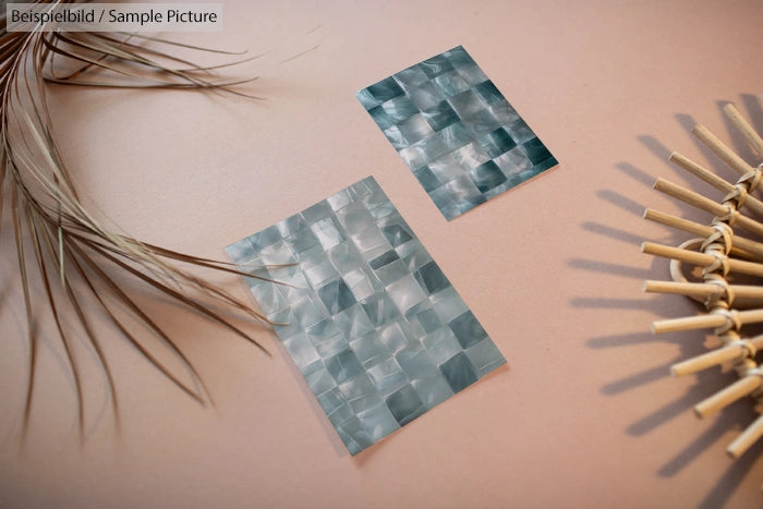 Two teal mosaic tile samples on beige background, with dried leaves and wicker fan decor.