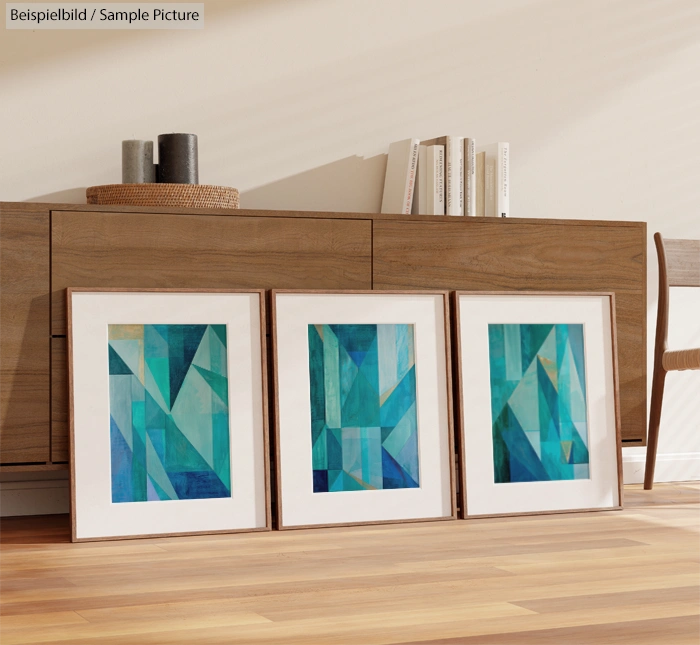 Three framed abstract paintings with blue and green geometric shapes displayed on a wooden floor by a sideboard.