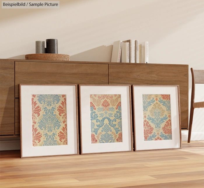 Three framed art prints with vintage floral patterns on wood floor, modern wooden sideboard in backdrop.