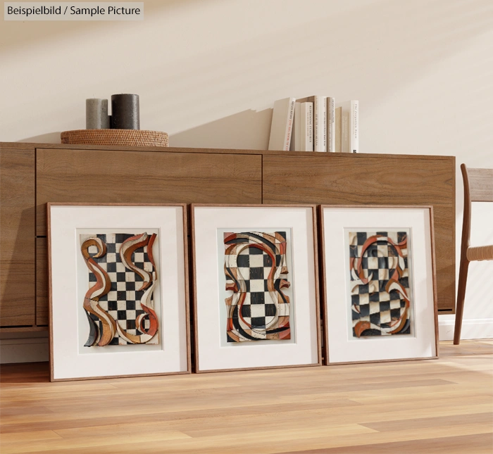 Framed abstract art prints with geometric patterns leaning against a wooden cabinet on a hardwood floor.