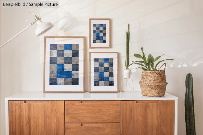 Modern living room with framed blue abstract art, potted plants and wooden sideboard against a white wall.