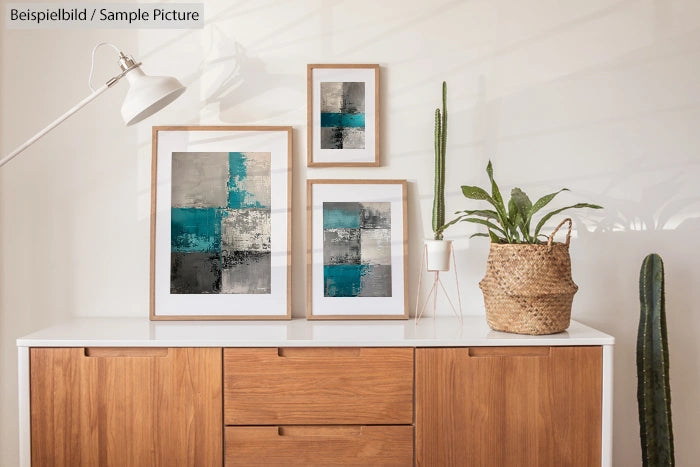 Modern living room with abstract framed art, wooden sideboard, and potted plants under a white lamp.