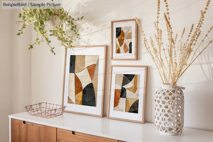 Minimalist decor with abstract art prints, wooden frames, woven vase, dried plants, and a basket on a wooden sideboard.