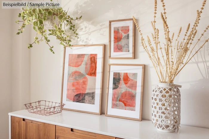 Modern interior shelf with abstract art in wooden frames, decorative vase, and hanging green plant.