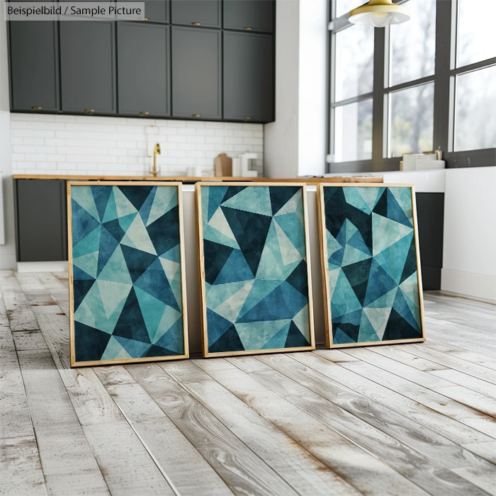 Three abstract geometric paintings with blue and teal triangles, leaning against a kitchen island with a white backdrop.