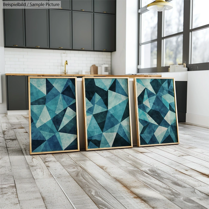 Three abstract geometric paintings with blue and teal tones on a kitchen floor, with modern cabinetry in the background.