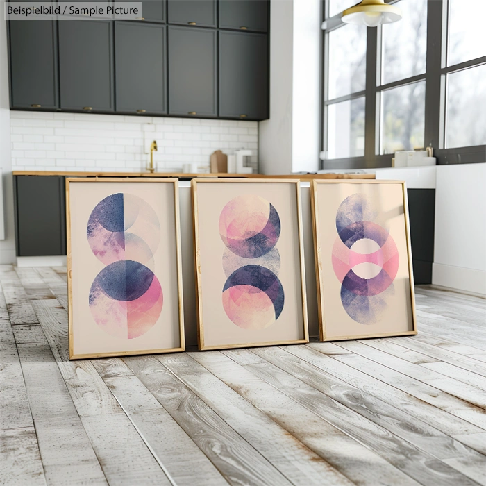 Framed abstract art with geometric patterns in pink, purple, and blue on kitchen floor with dark cabinets.