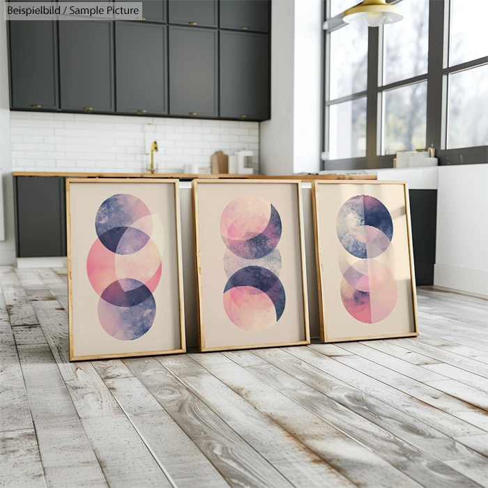 Three abstract art pieces with overlapping circles in pink and blue on display in a modern kitchen.