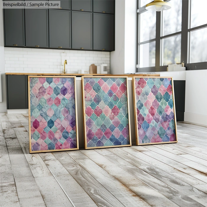 Three colorful abstract paintings with geometric patterns leaning against a kitchen island on a wooden floor.