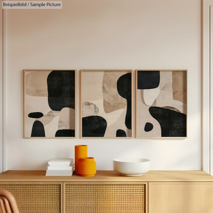 Abstract triptych artwork with black and beige shapes above a wooden console with decoration bowls.